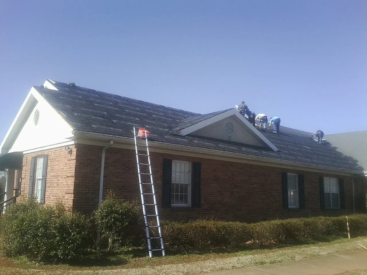 Crew tearing shingles off a brick ranch roof with a ladder set — Emergency Roof Repair work by our crew in Grovetown