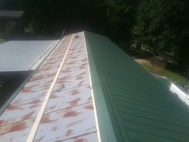 Old rusted panels beside newly installed green metal roofing — Wind Damage Roof Repair by Roofing Brothers in Grovetown