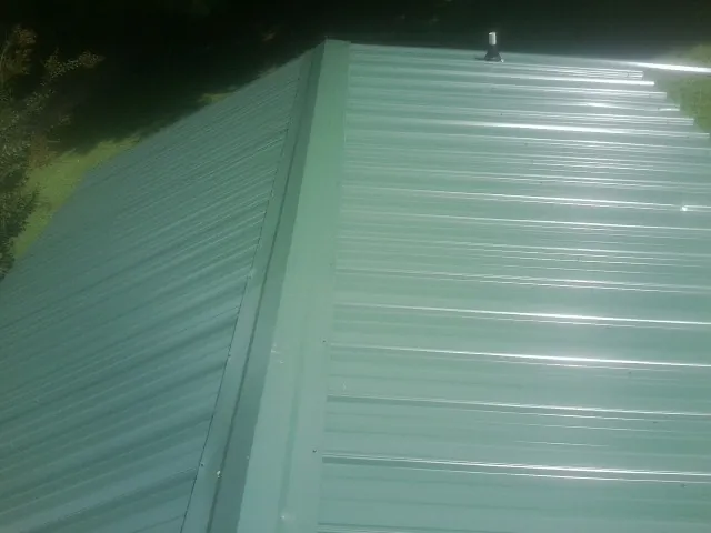 New green metal panels meeting at the ridge of a roof — Flat Roof Repair work by our crew in Grovetown