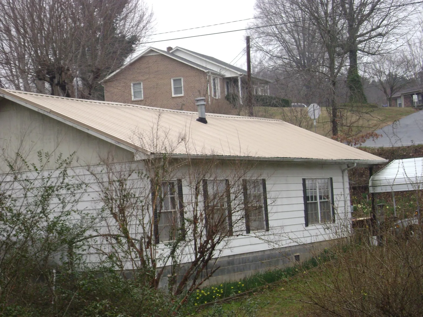 Tan metal roof on a white sided house set into a hillside — Commercial Roofing by Roofing Brothers in Grovetown